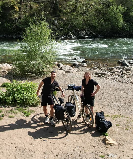 Two bicycle travelers in black sportswear posing with their bikes loaded with bags near a river surrounded by greenery in the Basque Country.
Turnkey bike holidays from The Family Bike.