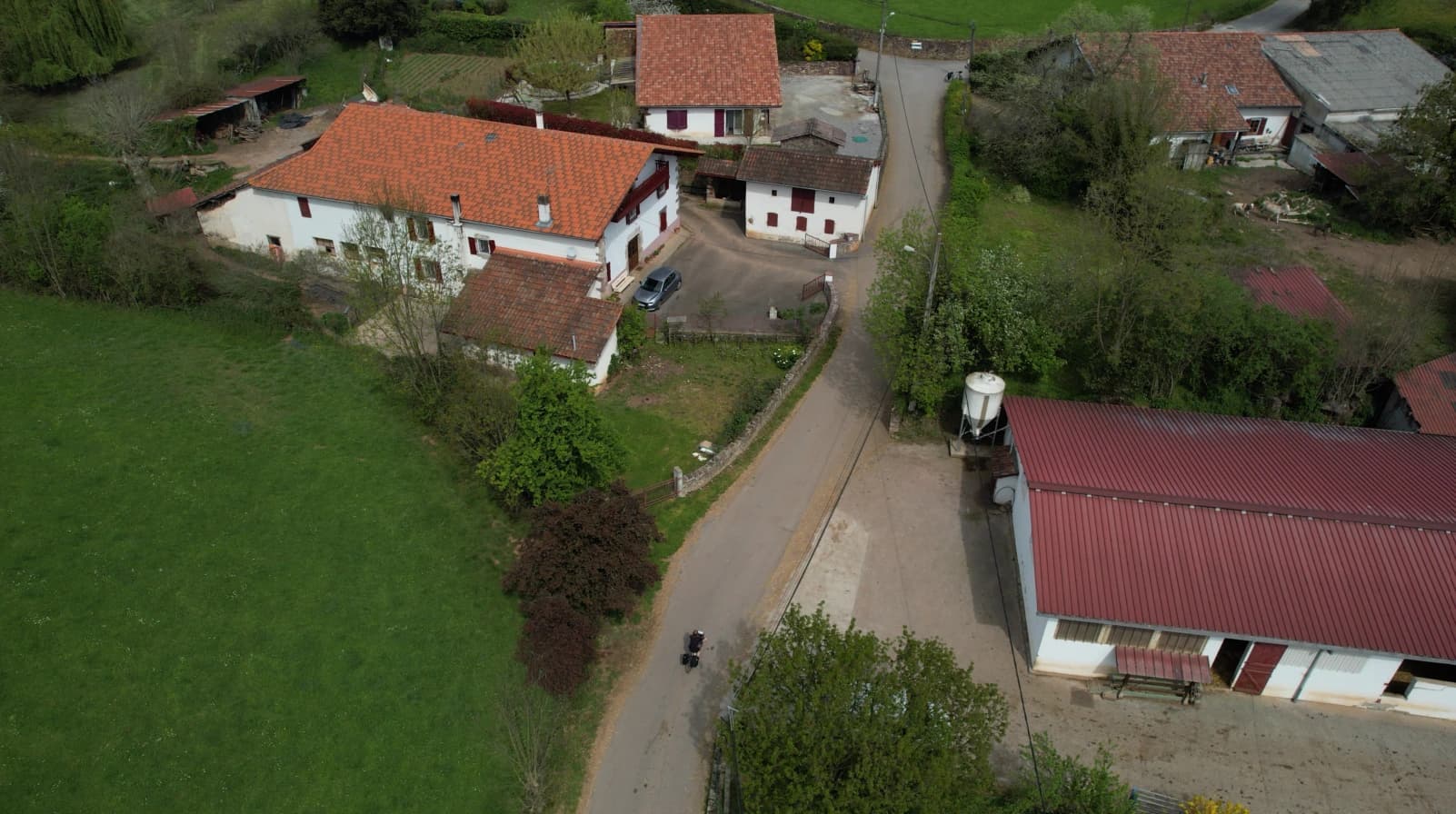 Vue aérienne d'un cycliste sur une route entre des maisons traditionnelles basques avec toits rouges et un champ vert.
Séjours à vélo clé en main de The Family Bike.